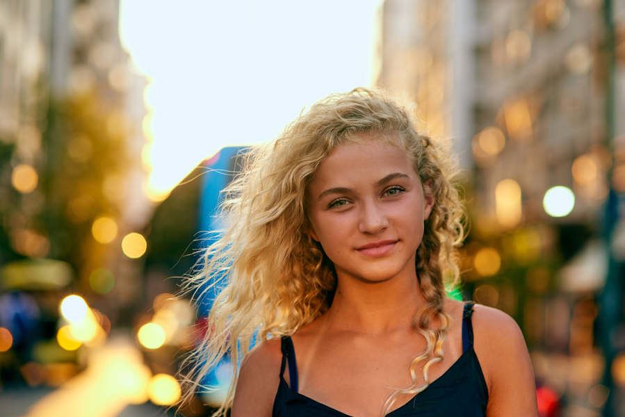 Outdoor portrait of a young woman with luminous velvet blonde hair, city background